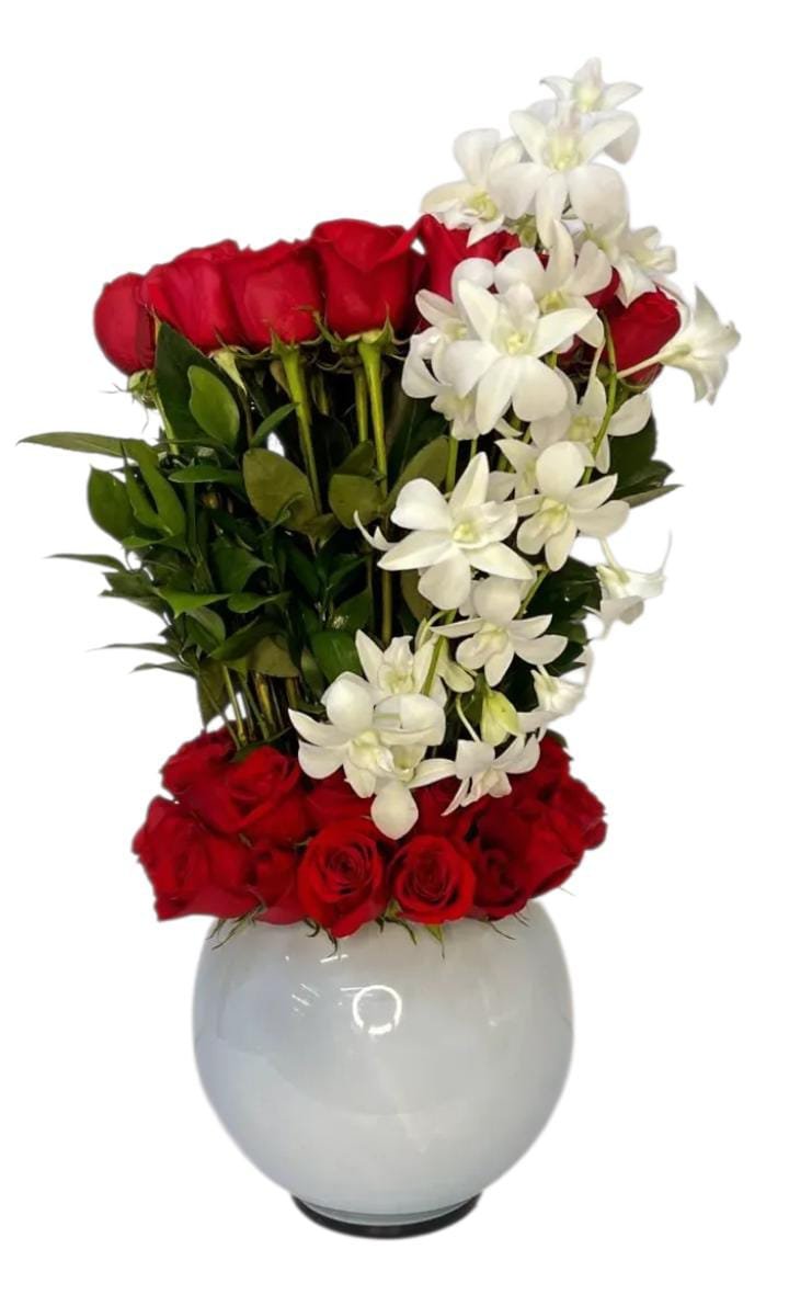 Arreglo floral elegante en florero blanco, con rosas rojas y orquideas, acompañado de follajes verdes